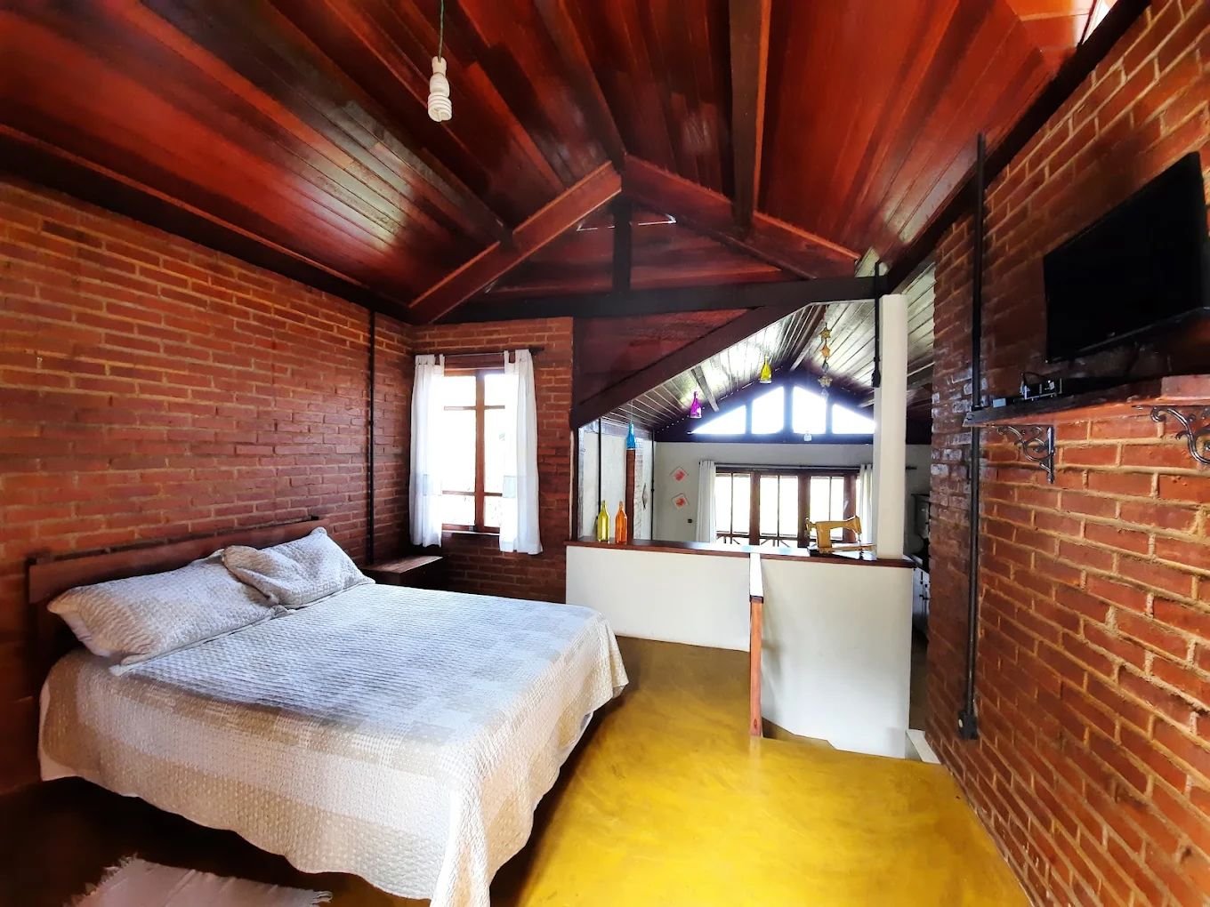 Quarto no mezanino com paredes de tijolo e teto de madeira