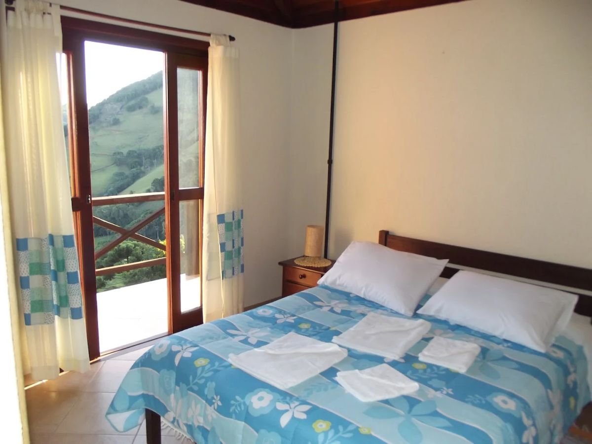 Quarto com porta de vidro aberta para a varanda e a encosta verde