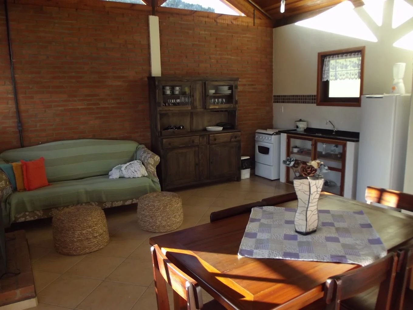 Sala integrada à cozinha, com sofá, cristaleira de madeira e mesa de jantar