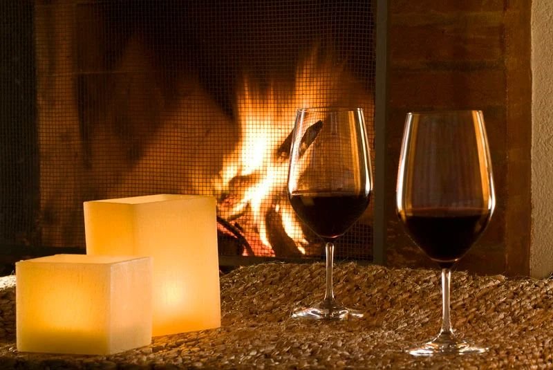 Duas taças de vinho tinto diante da lareira acesa, com velas